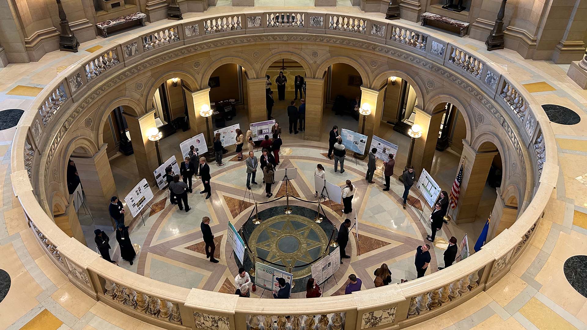 A view from above of posters on display in the Minnesota State Capitol rotunda. Posters are arranged around a large star pattern in the rotunda's floor