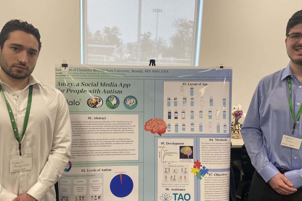 Two students stand in front of a poster explaining the process used to develop their idea for the Autzy app