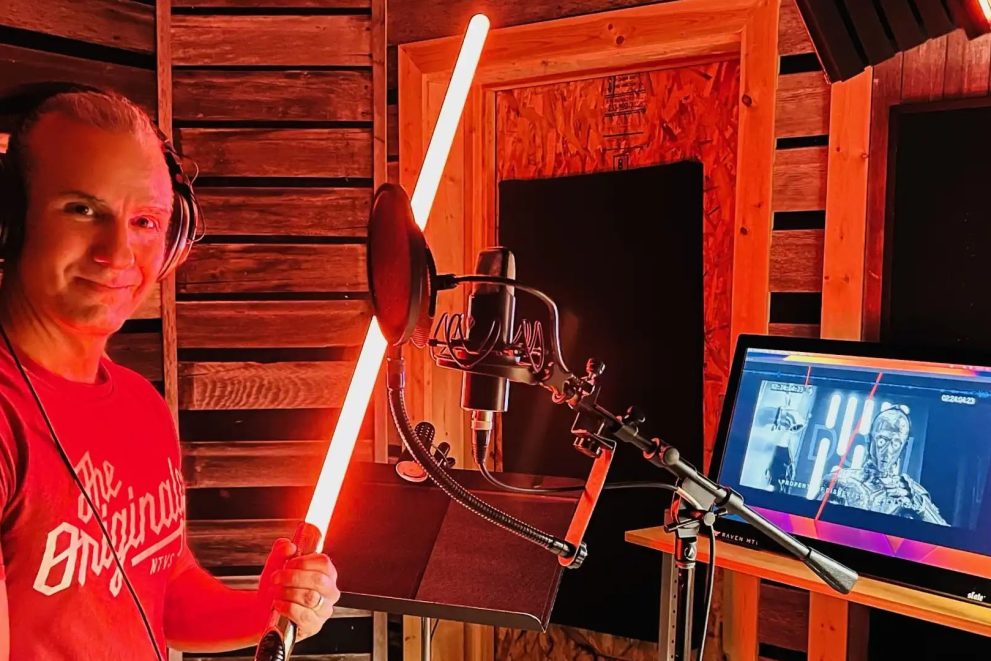 Dr. Anton Treuer, professor of Ojibwe, holds a red lightsaber in front of a microphone. a computer is open in front of him, and you can see C-3PO
