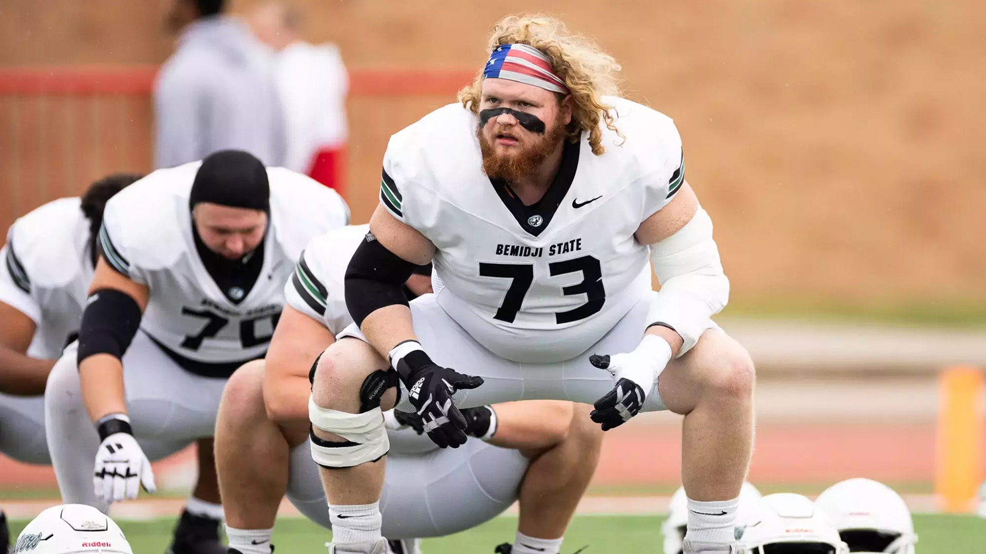  A BSU football player wearing jersey #73. He has long red hair and a red beard and is wearing a bandana that resembles an American flag