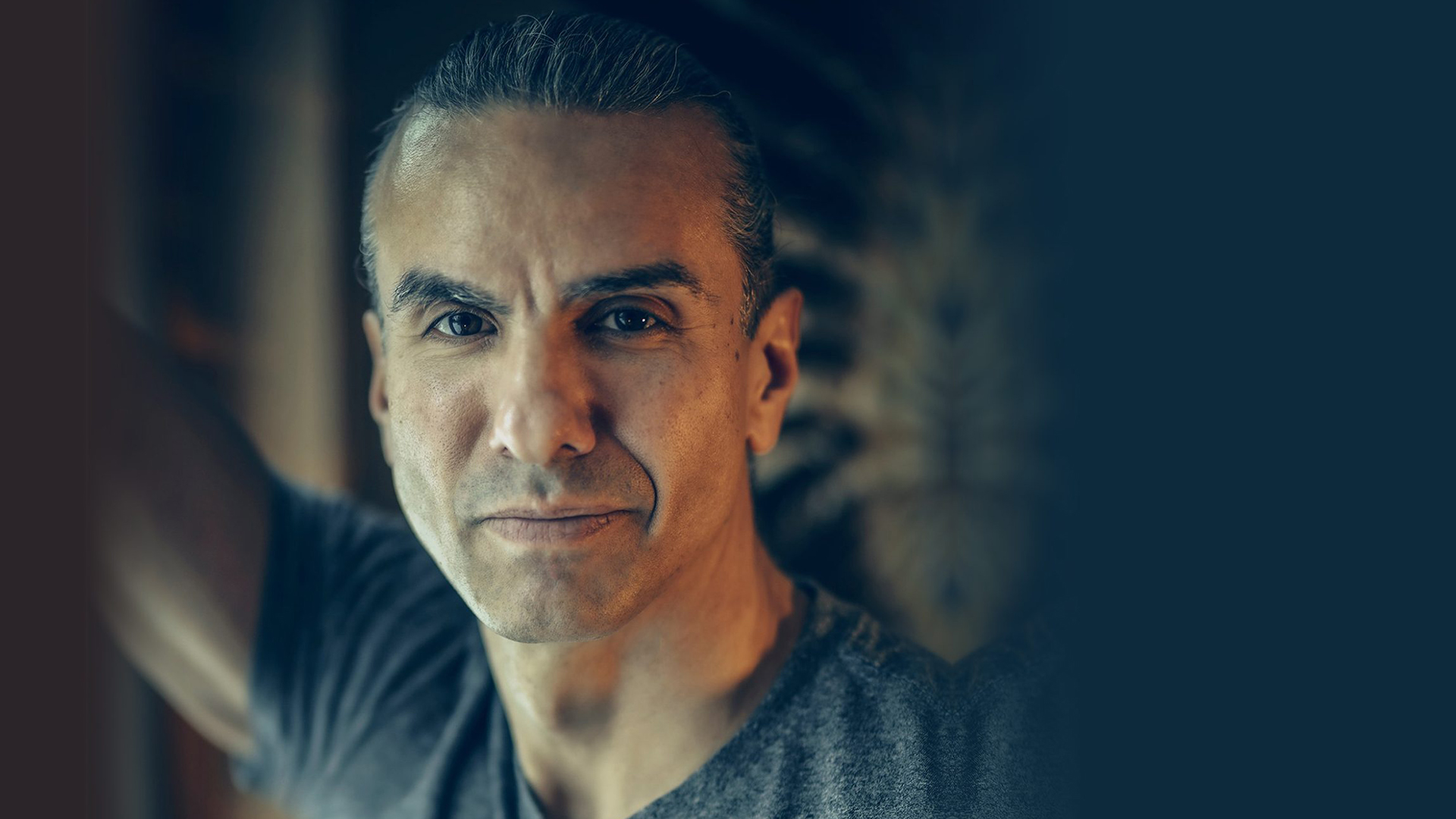 A portrait of Dr. Anton Treuer. His hair is pulled back in a pony tail and he's wearing a grey t-shirt.