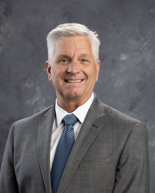A portrait of Christopher Waller wearing a grey suit and a blue tie.