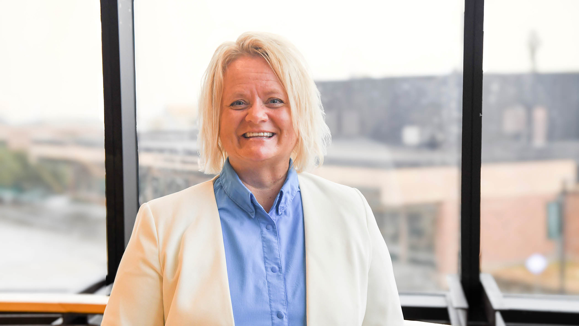 Dr. Marci Maple standing in the Memorial Hall stairwell overlooking the Hobson Union. Wearing a cream colored jacket with a blue shirt.