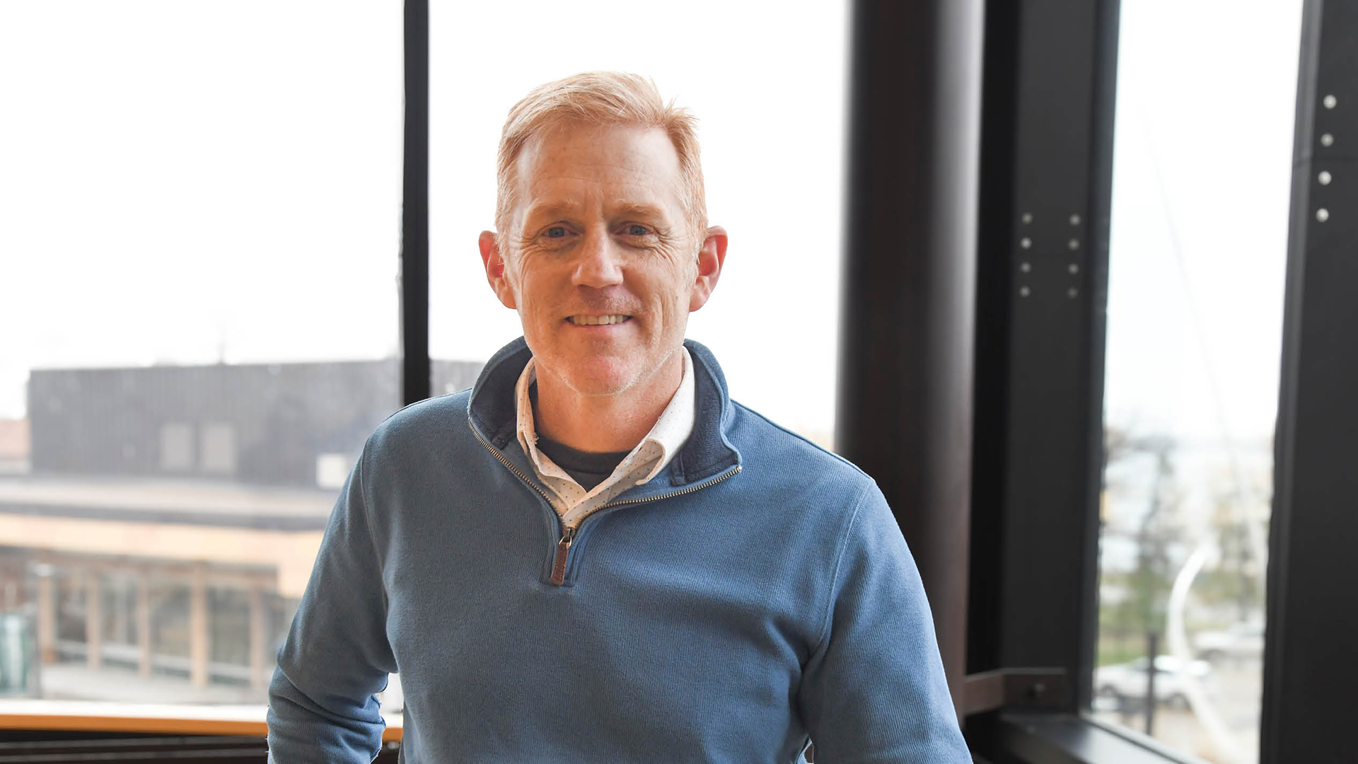 Dr. Travis Ricks in the Memorial Hall stairwell overlooking the Hobson Union. Wearing a blue quarter-zip pullover.