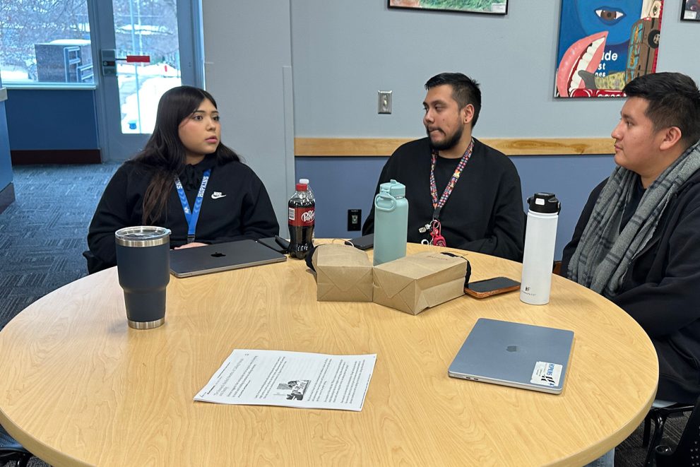 Three students are having a conversation at a round table.