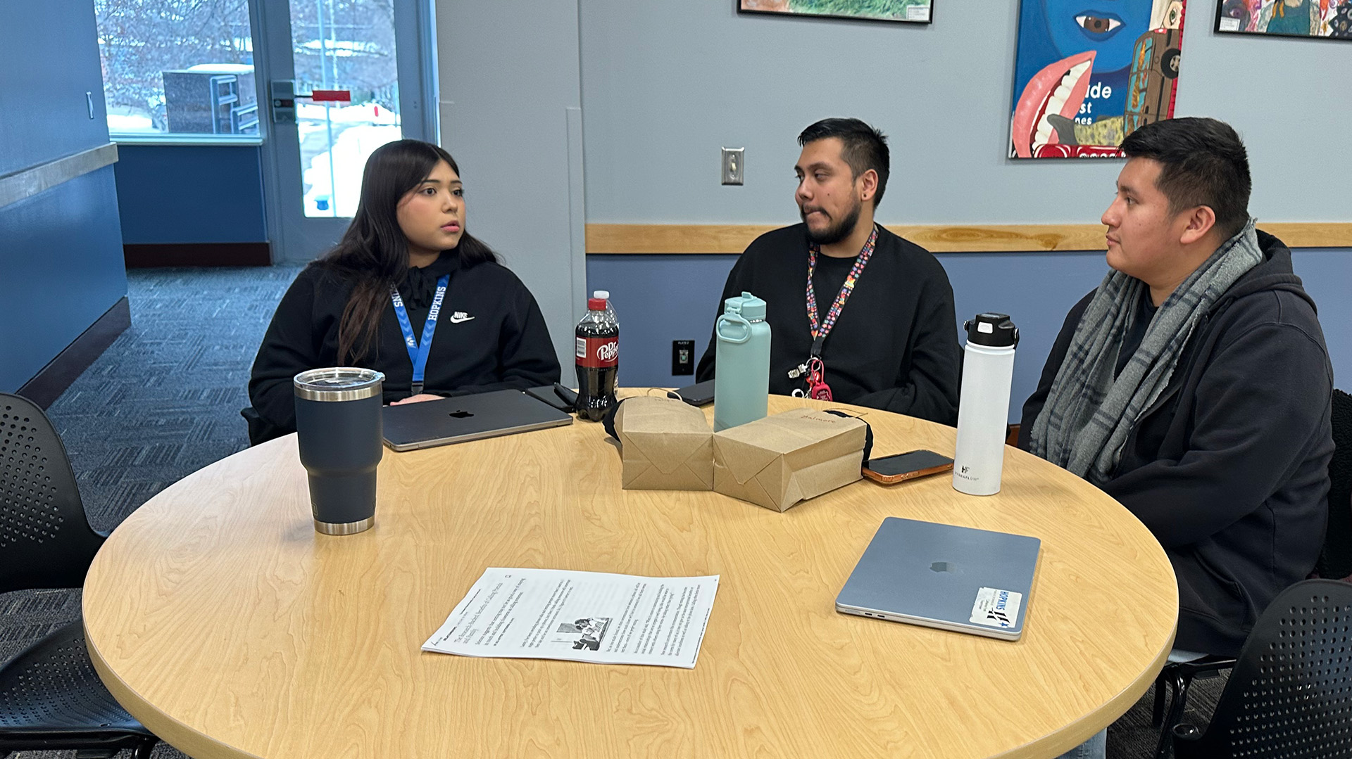 Three students are having a conversation at a round table.