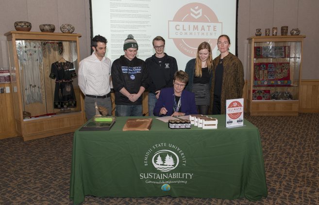 President Faith Hensrud signs Second Nature's Climate Commitment while Jordan Lutz, sustainability project manager, Connor Newby, student senate president, Corrie Stockman, student senate vice president, Anna Hayes, student senator and sustainability office employee and Erika Bailey-Johnson, sustainability coordinator, look on.