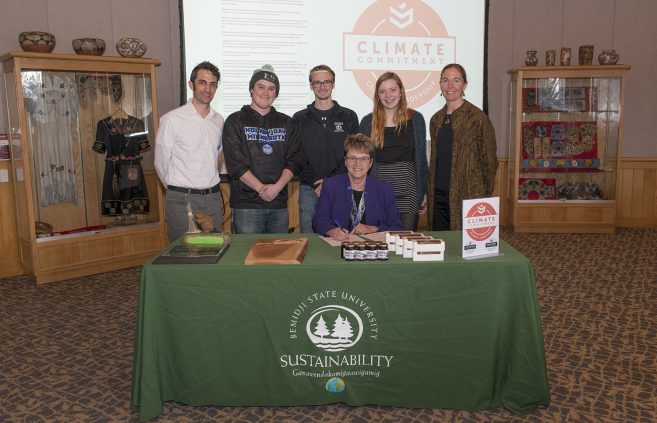 President Faith Hensrud signs Second Nature's Climate Commitment while Jordan Lutz, sustainability project manager, Connor Newby, student senate president, Corrie Stockman, student senate vice president, Anna Hayes, student senator and sustainability office employee and Erika Bailey-Johnson, sustainability coordinator, look on.