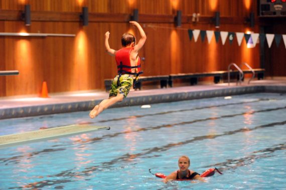 A young boy in a life jacket jumping into a pool