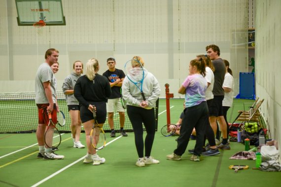 BSU students huddled around on a tennis court