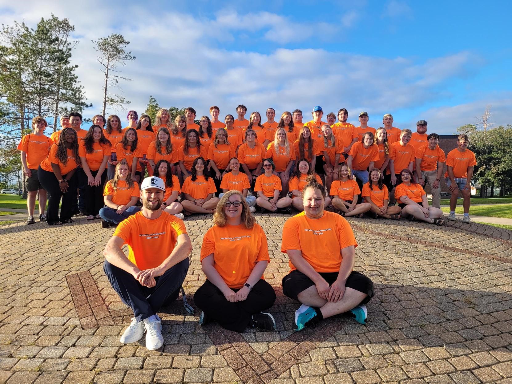 Housing & Residential Life student staff group picture with the three Area Directors in the front on top of the mound outside of Tamarack Hall. 
