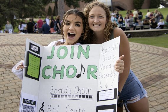 Two students holding a join choir sign