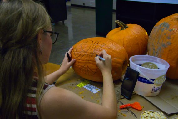 Student drawing a design on a pumpkin