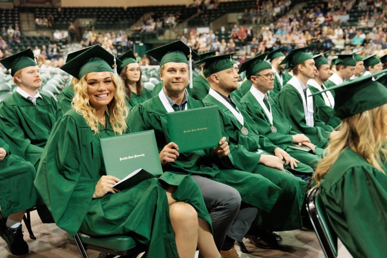 Bemidji State students in green robes holding up their diplomas in the Sanford Center