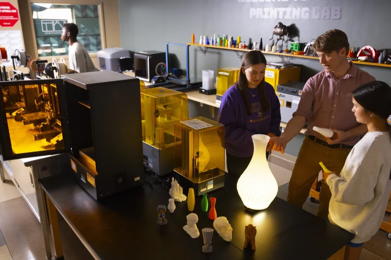 Students standing around a 3-d printed vase with a professor